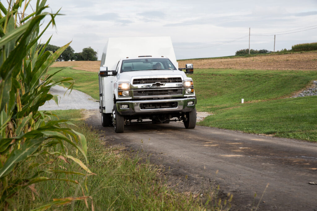 White HooverTec service truck driving in a lane past cornfields.